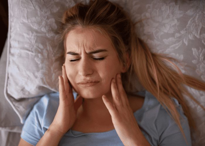 teenage girl in bed rubbing jaw in pain caused by teeth grinding in teens