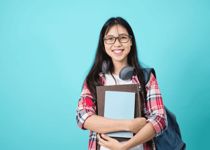 Teenage girl holding schoolbooks and rucksack smiling after treatment for fidgeting in teens