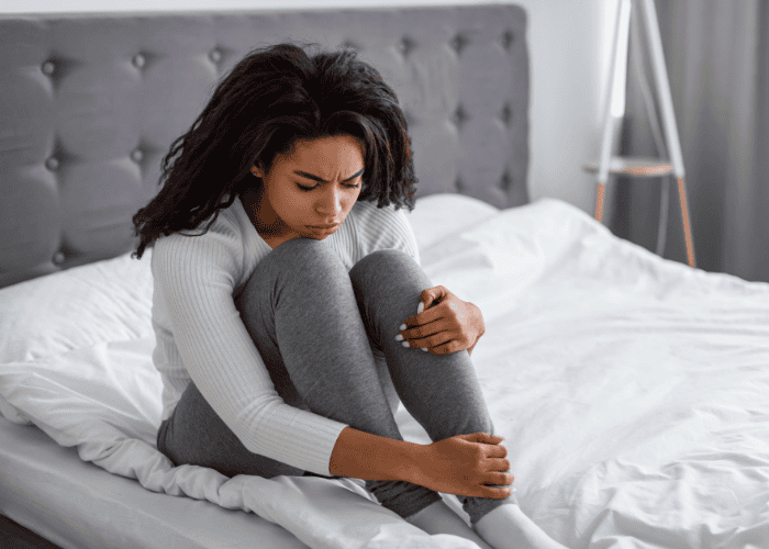 Teenage girl sitting on bed looking anxious due to bedtime anxiety in teens