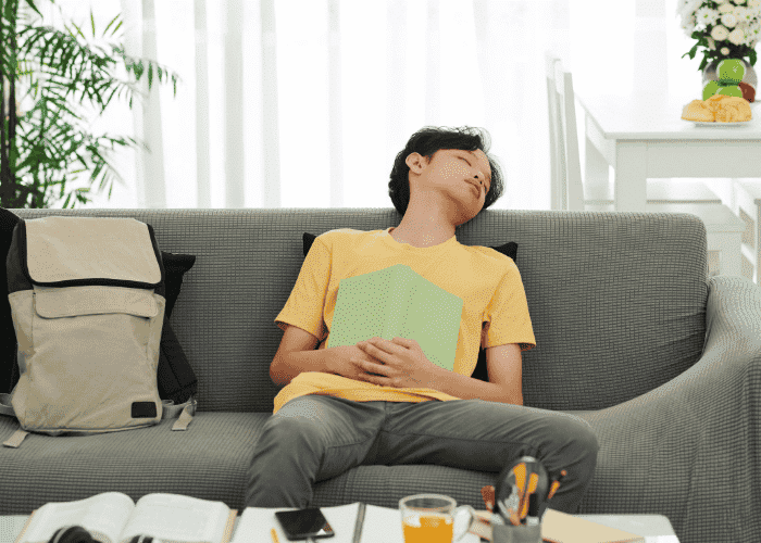Teenage boy asleep on sofa holding a book due to daytime sleepiness in teens