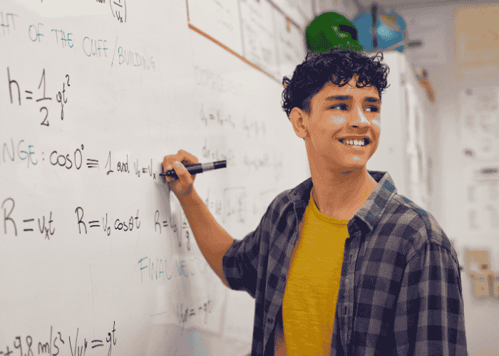 Teen boy smiling whilst completing math calculation on whiteboard in class after support with information overload in teens