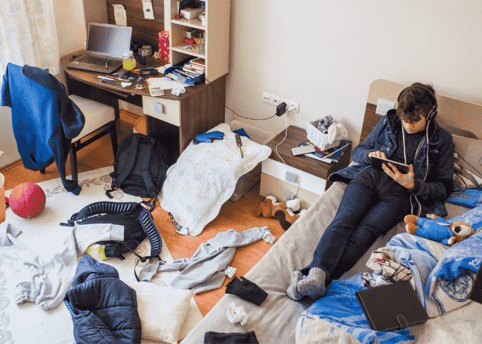 Teen boy avoiding responsibilities listening to music in messy bedroom