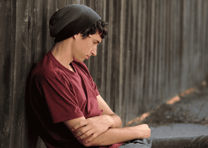 Teen say outside leaning against fence due to pulling away after an argument.