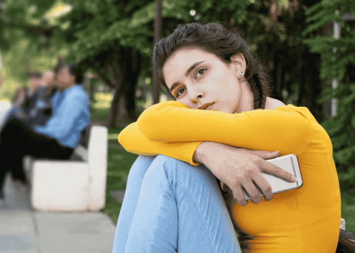 Teenage girl sitting outside experiencing dissatisfaction with life in teens