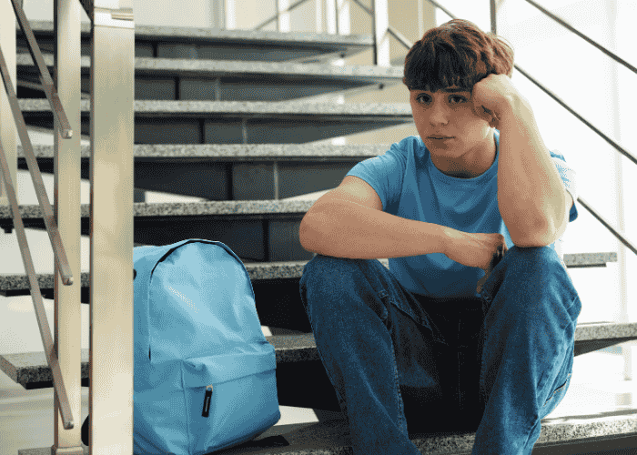 Teenage boy sitting on steps looking unhappy experiencing anhedonia in teens