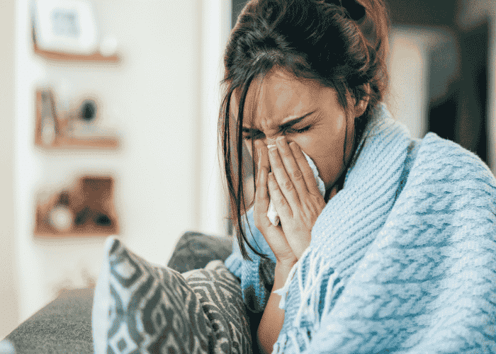 Teenage girl blowing her nose covered in a blanket wondering why teens can get sick often