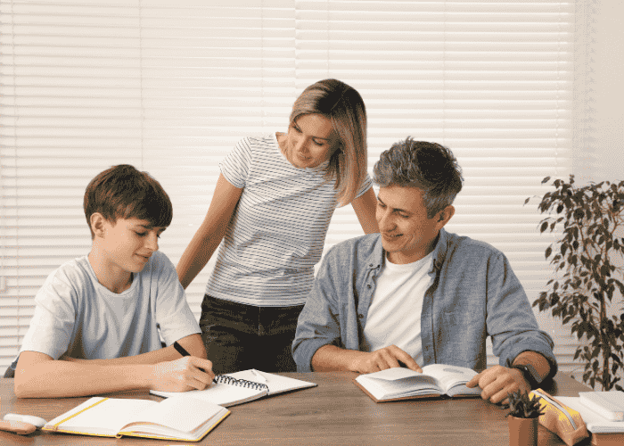 Teenage boy doing schoolwork happily with his parents after receiving treatment for feeling like a burden