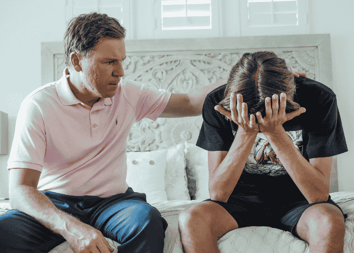Teenage boy sitting with his dad with his head in his hands due to avoiding eye contact in teens