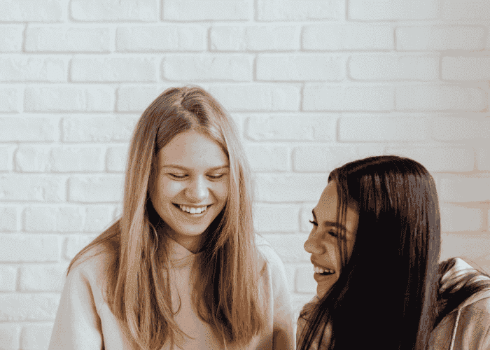 Two teenage girls laughing together after receiving treatment for oversharing in teens