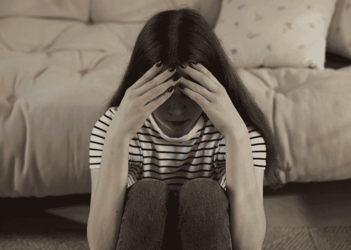 Teenage girl sitting on the floor with her knees to her chest and head in her hands due to anxiety & faint feelings in teens