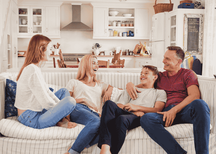 Mom and dad sitting on sofa with teenage kids smiling and laughing after seeking support with mental health insurance cover