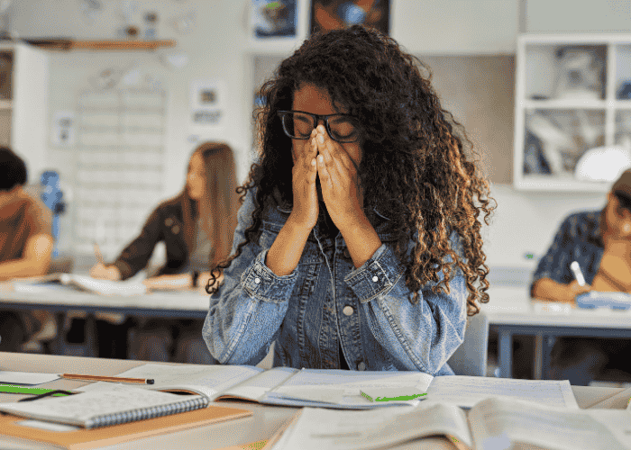 teen girl experiencing anxiety at school sitting at desk with hands over face needing support from The Holman Group Insurance Coverage