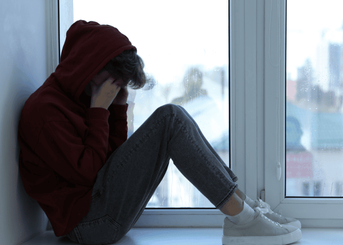 Teen sitting on floor with back against wall hiding face in hands needing support from TRICARE Mental Health Coverage