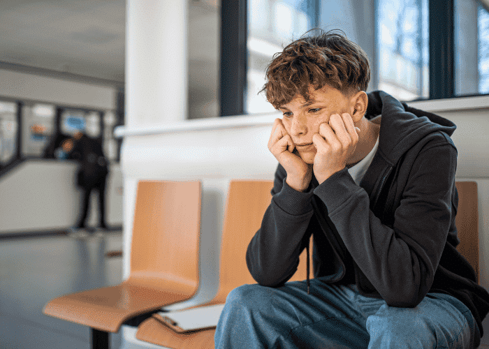 teen boy sitting on chair in corridor looking anxious with head in hands before starting Acceptance and Commitment Therapy