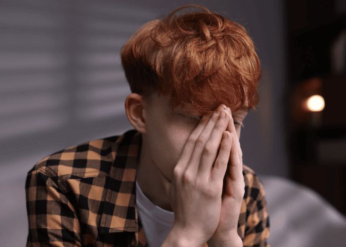 Teen boy sitting on his bed looking panicked with hands cupped over mouth, needing support with ComPsych mental health insurance