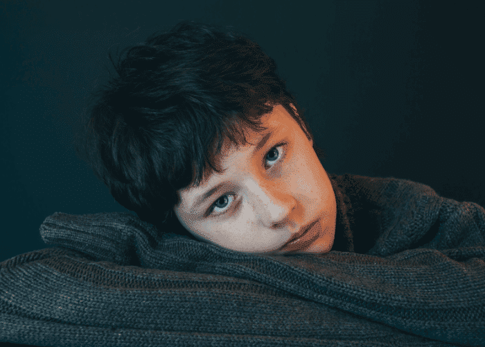 Teen boy laying with arms crossed and head resting on arms looking worried about seeking support with First Health Network Mental Health Insurance