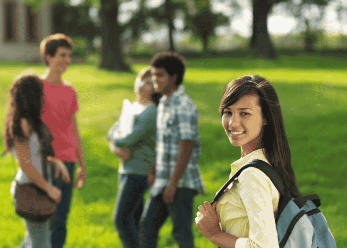 Teen girl walking to school with friends across park smiling after support with First Health Network Mental Health Insurance