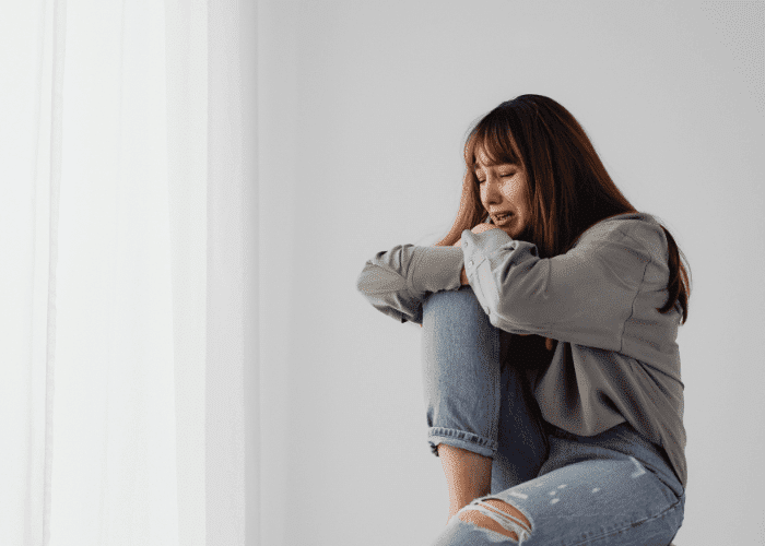 Teen girl sitting on chair with leg pulled towards chest crying and wanting a better understanding of teen neurodivergent brains and emotional experiences