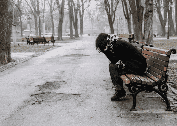 Teen sitting on park bench alone, leaning forward with head in hands wanting to know more about how shame affects neurodivergent teens