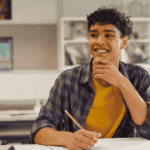 teen boy at school sitting at desk working and smiling after seeking support with why sensory overload in teens feels like panic