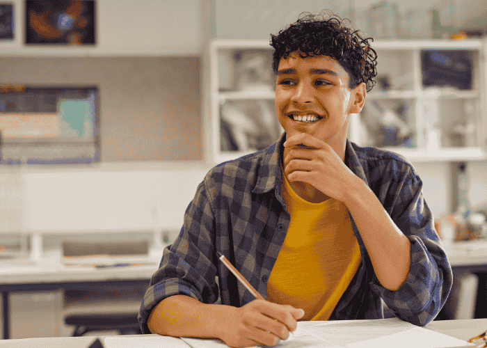 teen boy at school sitting at desk working and smiling after seeking support with why sensory overload in teens feels like panic