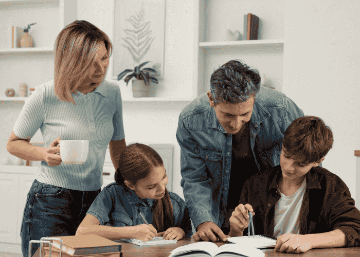 Happy teenage boy and girl completing homework at table with mom and dad after seeking support with Carelon mental health coverage