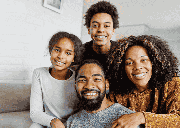 Teen boy in lounge with mom, dad and sister, smiling after treatment for complex PTSD in teens