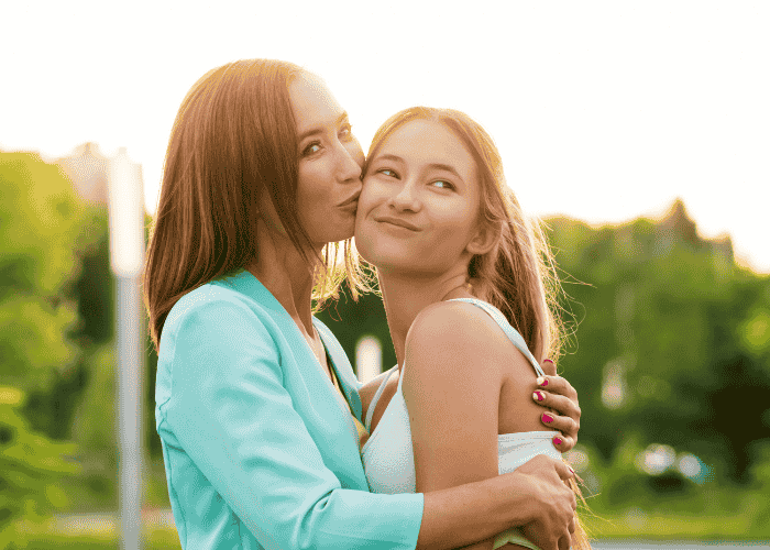 mom kissing smiling teen daughter on cheek outside in garden after seeking support with HMC HealthWorks