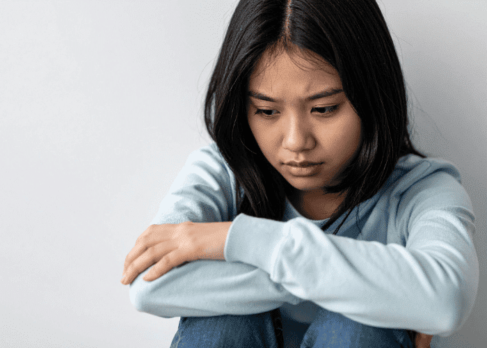 teen girl sitting against wall resting her arms on her raised knees worrying about Kaiser mental health insurance