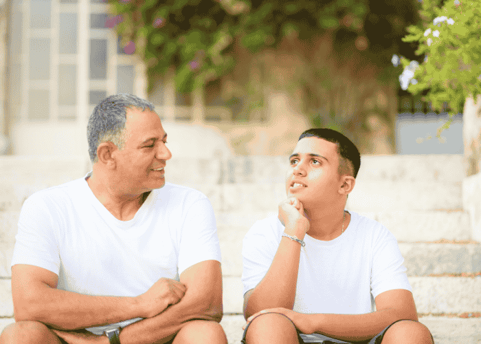 Father sitting with boy on steps outside smiling after seeking support with Kaiser mental health insurance