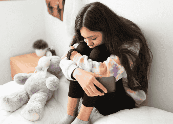 Teenage girl sitting on bed with legs pulled to chest wondering when is the right time to talk to someone about your mental health.