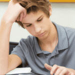 Teenage boy sitting at desk with head resting on hand worrying his friend is not coping with mental health issues