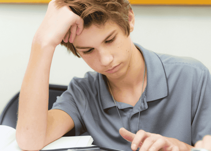 Teenage boy sitting at desk with head resting on hand worrying his friend is not coping with mental health issues