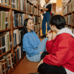 Teenage girl sitting on floor in library chatting to friend about coping with mental health issues