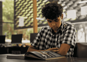 Teenage boy sitting at desk with arms crossed looking down needing support with changes to youth mental health treatment