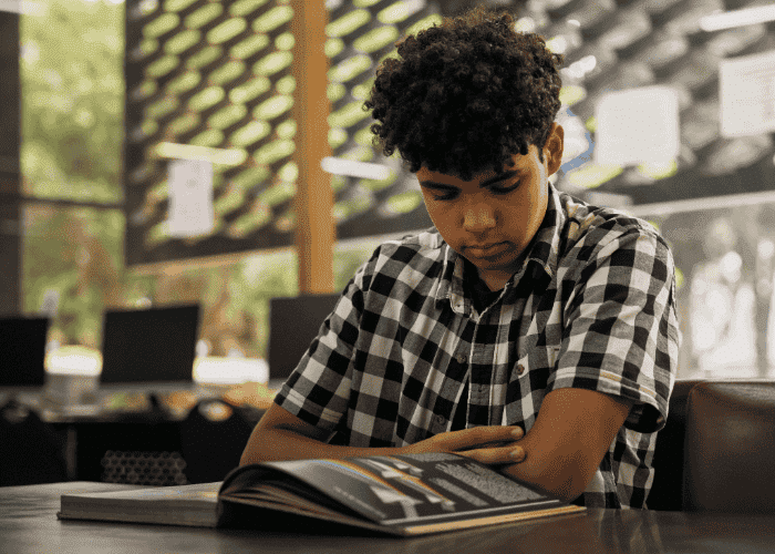 Teenage boy sitting at desk with arms crossed looking down needing support with changes to youth mental health treatment