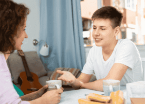 Teen boy sitting at table with mom smiling after receiving support with changes to youth mental health treatment