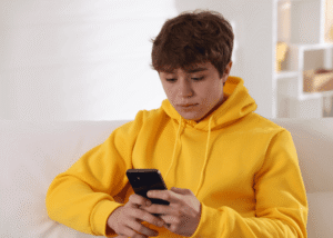 Teenage boy sitting on sofa looking at phone experiencing teen climate anxiety