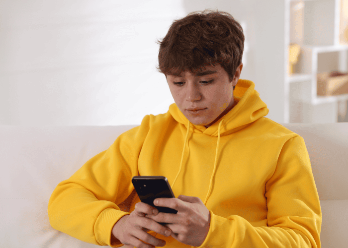 Teenage boy sitting on sofa looking at phone experiencing teen climate anxiety