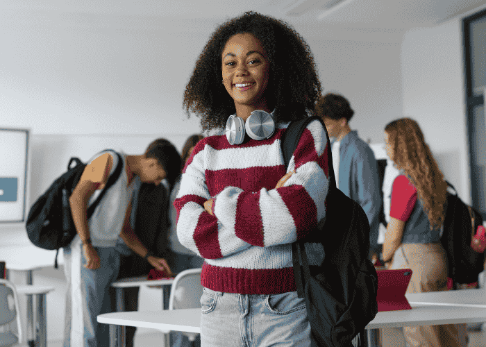 Teenage girl in classroom standing with arms crossed smiling after receiving support for teen climate anxiety