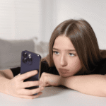 Teenage girl leaning on table with chin resting on arm using phone in line with Virginia's new screen time law.