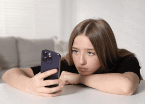 Teenage girl leaning on table with chin resting on arm using phone in line with Virginia's new screen time law.