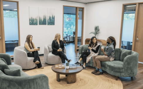 Four people engaging in group therapy in a comfortable, home-like residential lounge.
