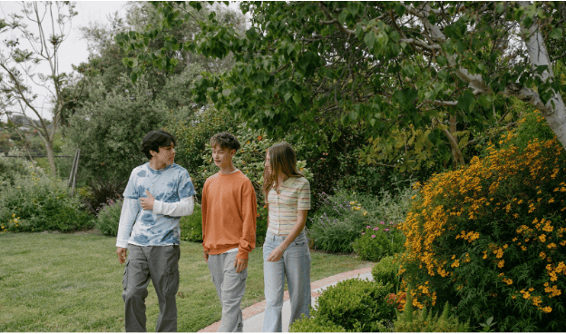 Three smiling teenagers walking together outdoors in a garden with lush greenery.