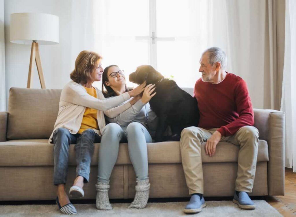 Family sitting together on couch in living room petting their dog