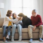 Family sitting together on couch in living room petting their dog
