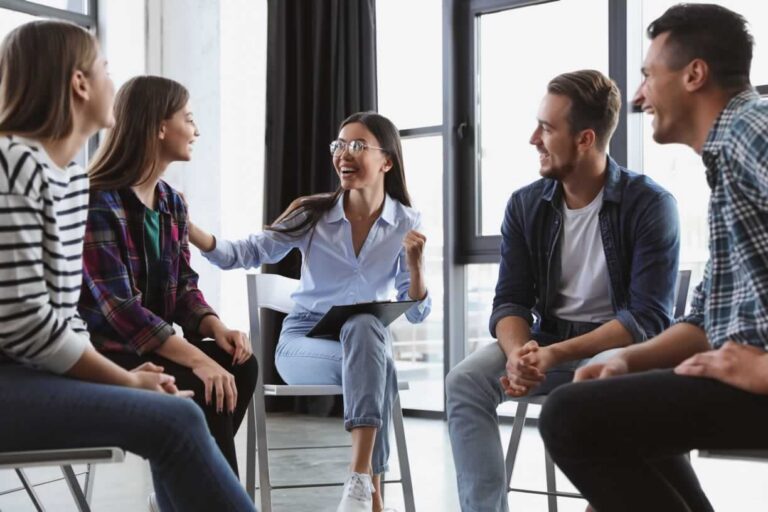 Male and female teens smiling as they sit in chairs in a circle and participate in group therapy
