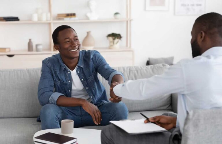 Young man sitting on couch shaking the hand of therapist who sits across from him