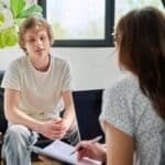 Teen boy sitting on chair across from female therapist during therapy session