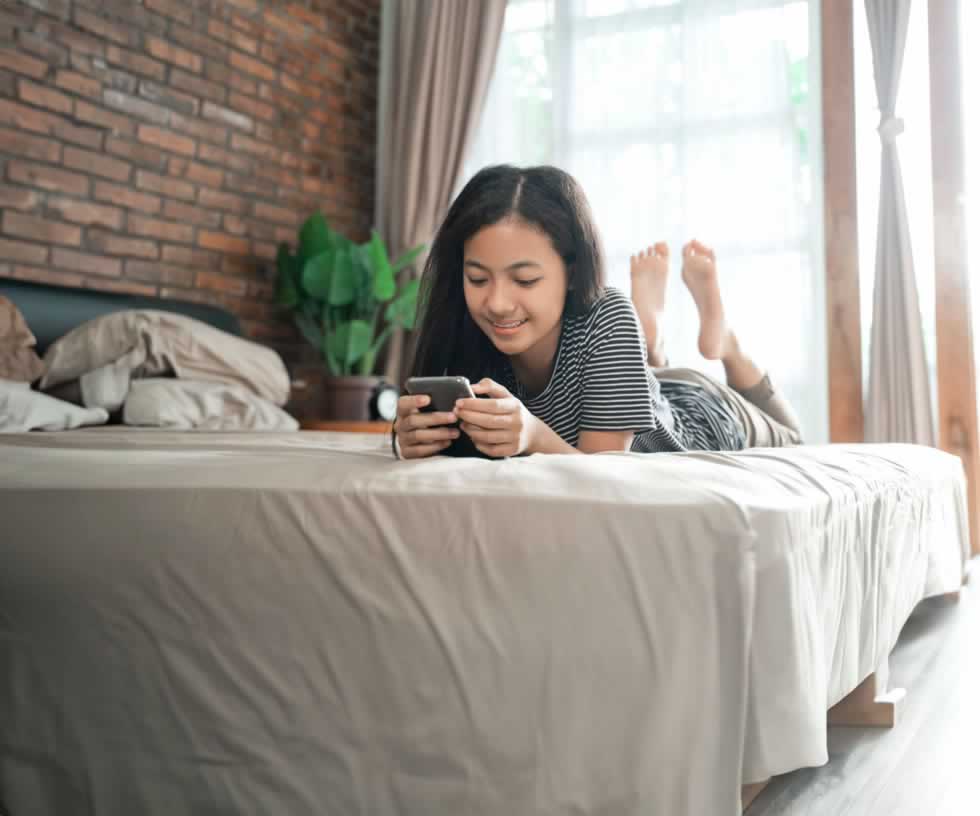 Teen girl lying on bed while looking at phone and smiling